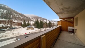 A balcony with a view of a snowy mountain, a small stone building, and a wooden cabin.