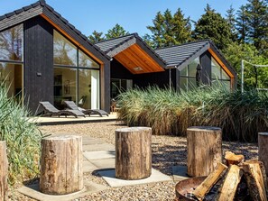 Une maison moderne dotée de grandes fenêtres, d’un patio avec des fauteuils et d’un foyer extérieur.