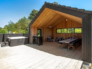Eine Holzterrasse mit Whirlpool, Bar und Essbereich mit Gartenmöbeln.