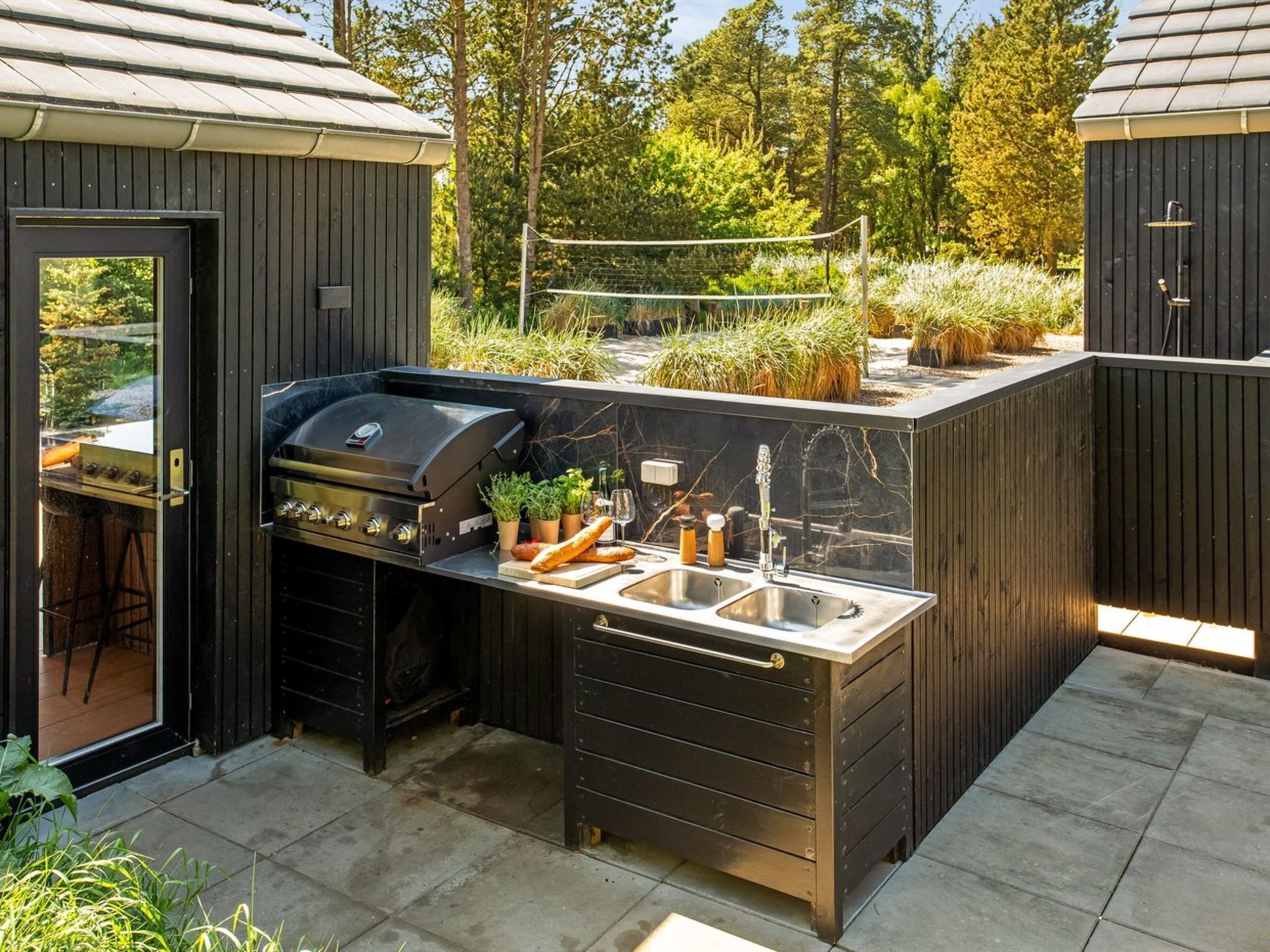 A modern outdoor kitchen with a built-in grill, a sink, and a small countertop.