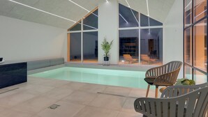 Ein moderner Poolbereich im Innenbereich mit großen Glaswänden, einer Lounge mit Stühlen und einer Rezeption.
