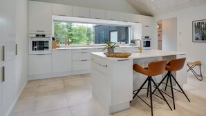 Eine moderne Küche mit weißen Schränken, einer großen Kochinsel mit Barhocker und Blick ins Freie.