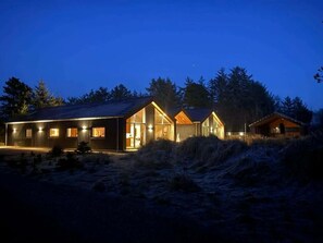 Eine moderne Hütte mit großer Glasfassade, Holzaußenverkleidung und einem gut beleuchteten Eingang.