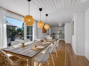 Un espace de salle à manger moderne avec une table en bois, des chaises blanches et des suspensions en fibres tressées.