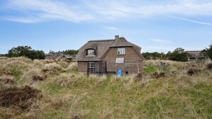 Ein traditionelles Haus mit einem Reetdach, umgeben von hohem Gras und Bäumen.