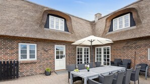 Eine Terrasse mit Tisch und Stühlen, einem weißen Sonnenschirm und einer Ziegelwand mit Fenstern.