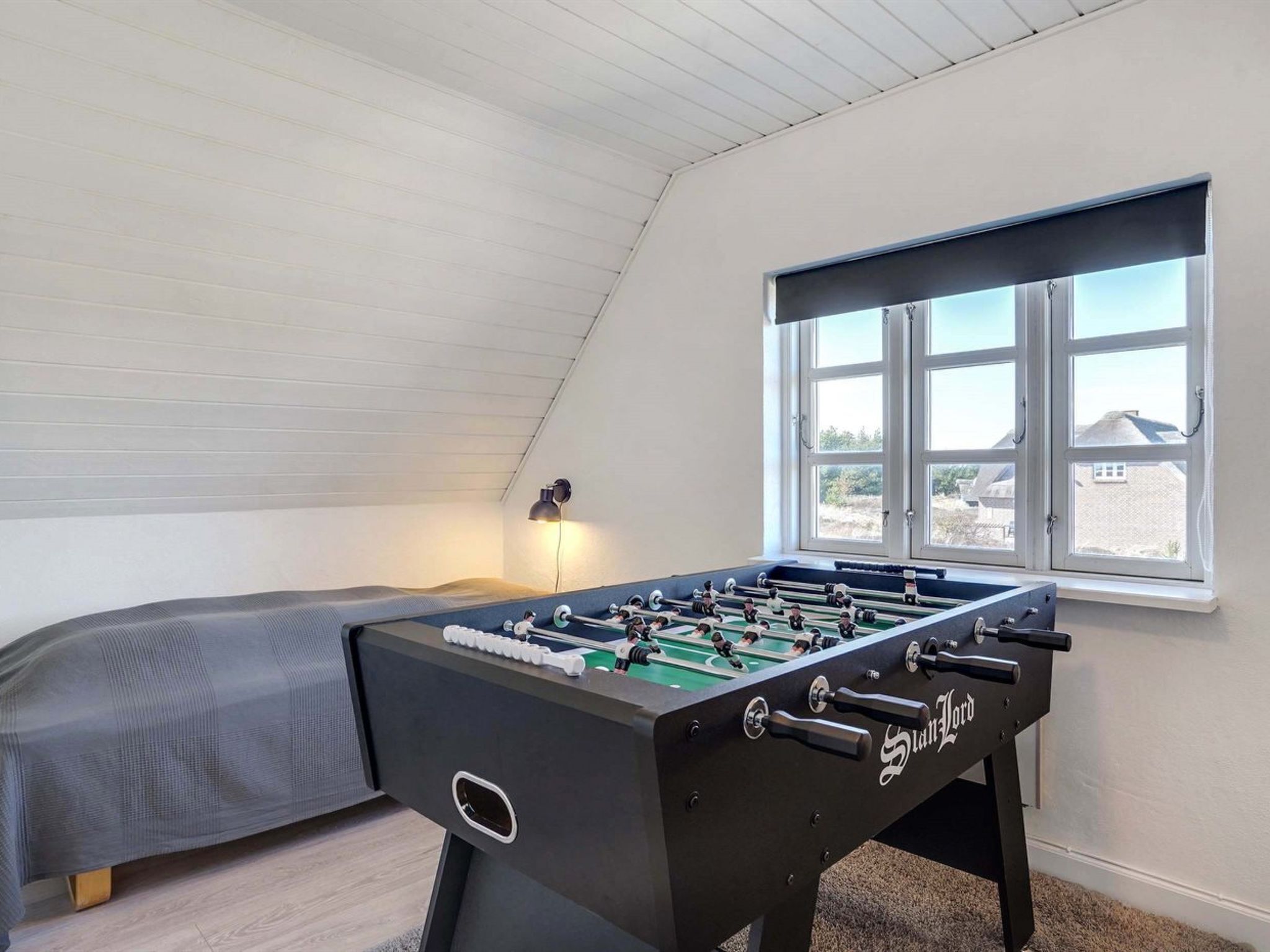 Une pièce avec une table de baby-foot, un lit et une fenêtre donnant sur des maisons.