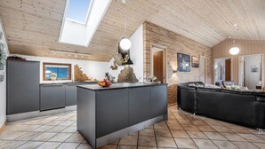 Eine moderne Küche mit einer zentralen Kochinsel, einem Essbereich mit einer schwarzen Ledersofa und einer Loft-Decke mit Holzbalken und Dachfenstern.