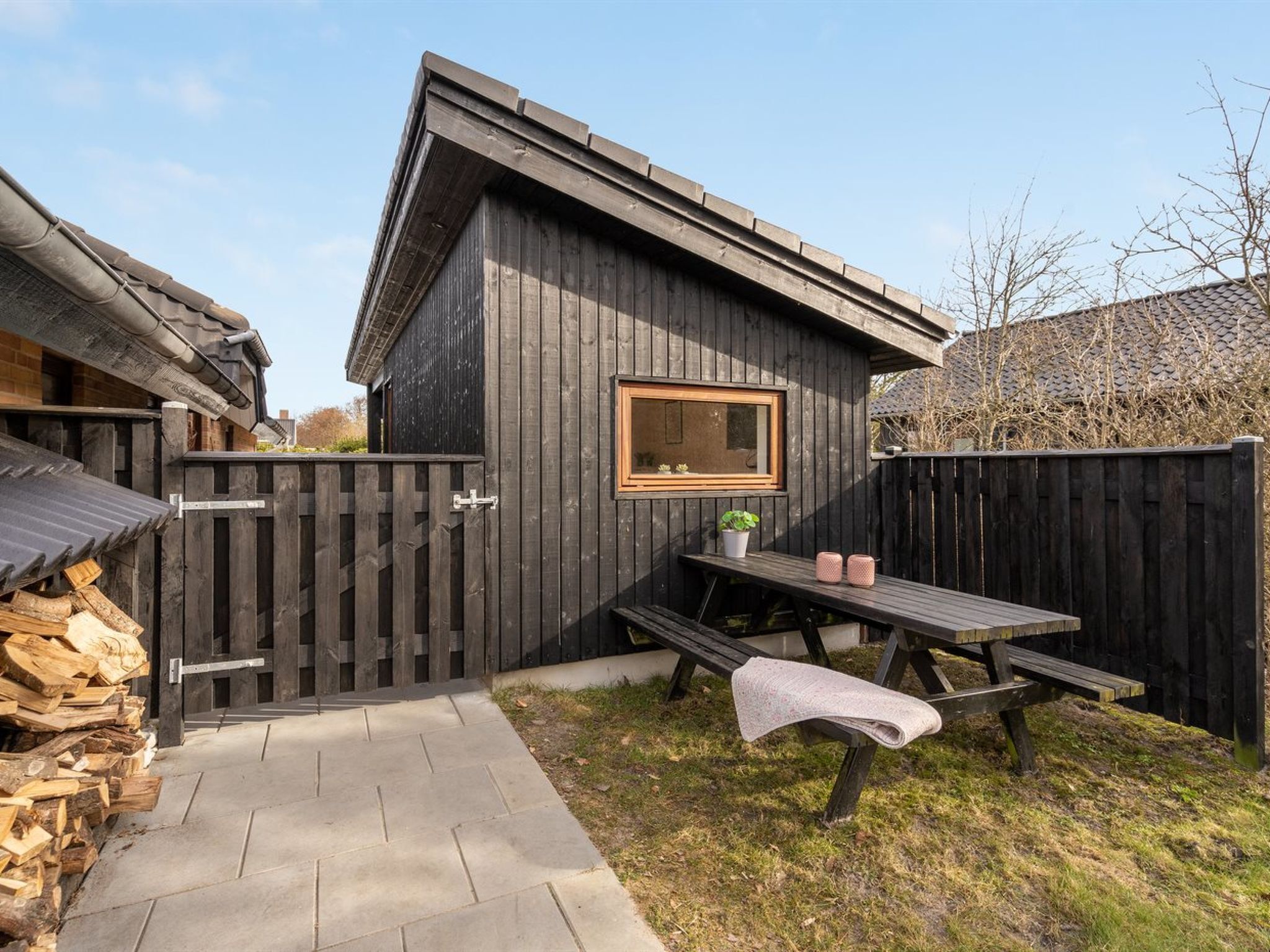 A wooden cabin with a picnic table and bench, a small window, and a wooden fence.