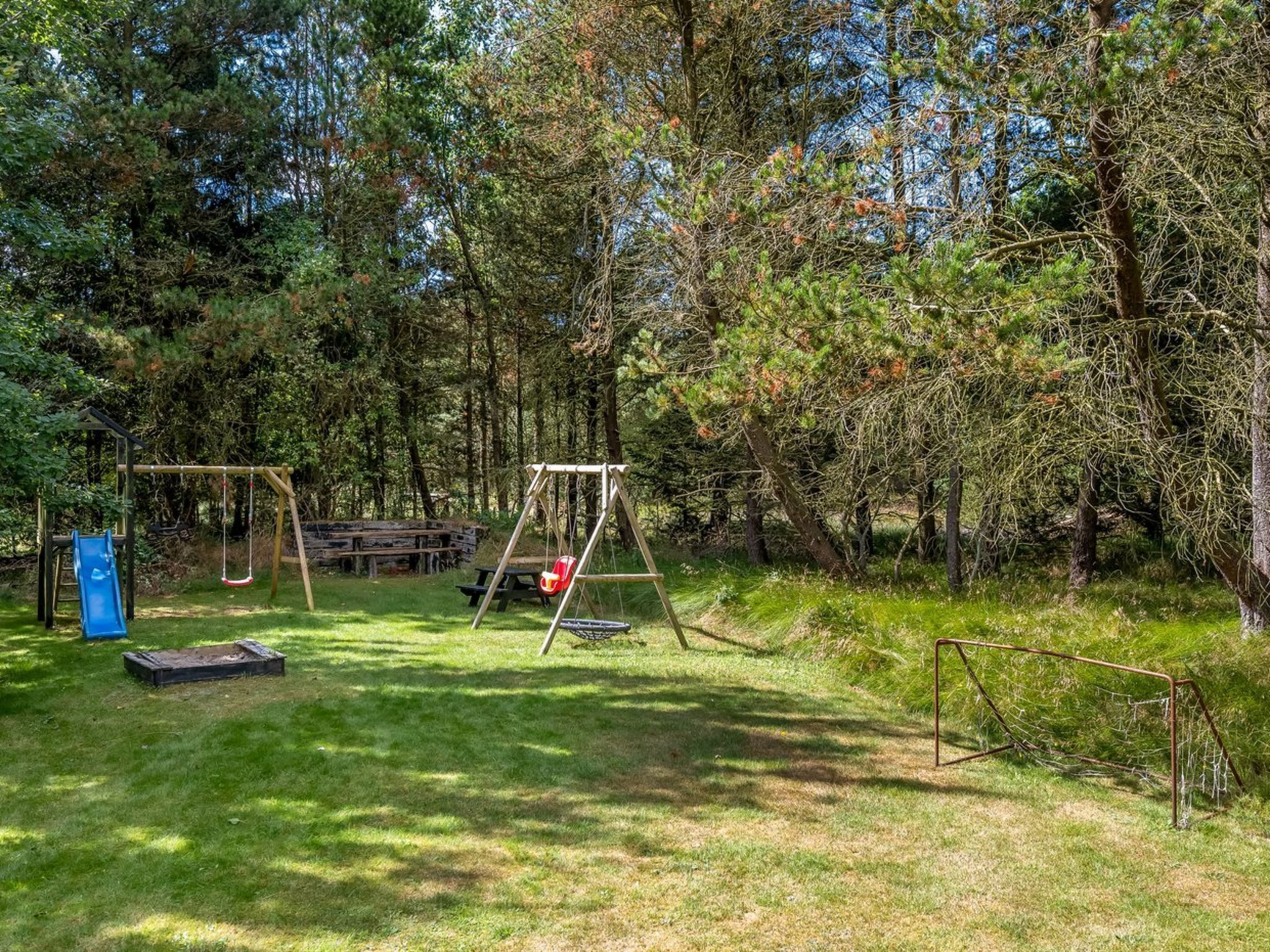 En legeplads med gyngestativ og rutschebane i et skovområde.