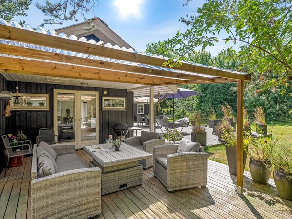 An outdoor patio with wicker furniture, a pergola, and potted plants.