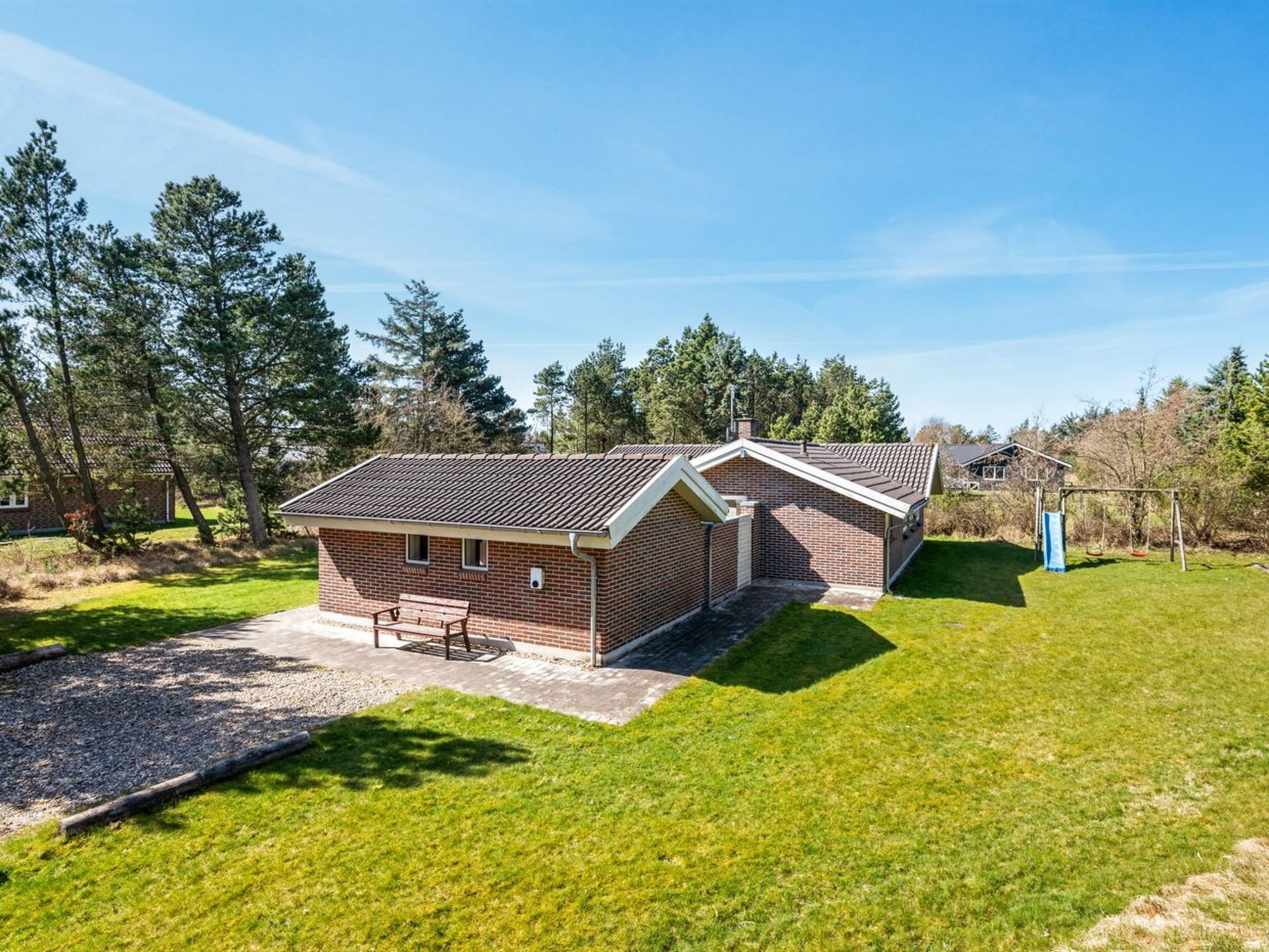 A two-story brick building with a sloped roof, a small patio with a table and chairs, and a swing set in the yard.