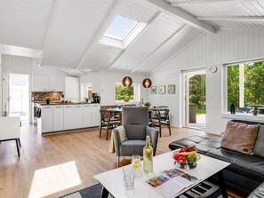 Un espacio habitable amplio con mesa de comedor, sofá y zona de cocina con armarios blancos.