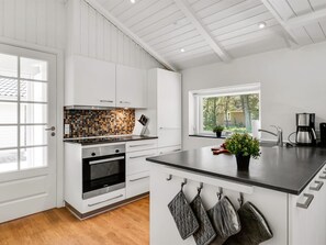 Una cocina moderna con armarios blancos, salpicadero de azulejos y un ventanal grande.