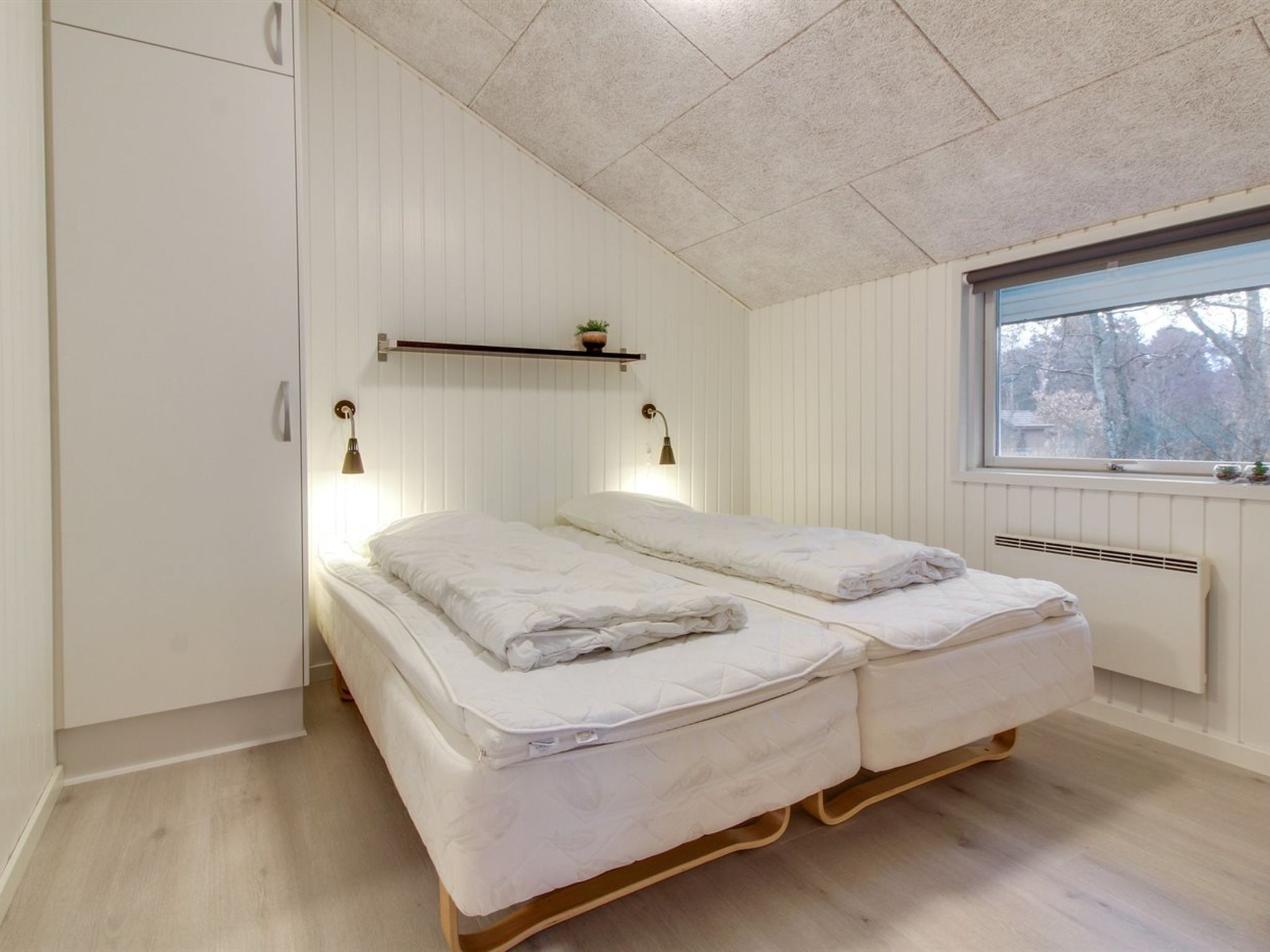 Un dormitorio con dos camas, una ventana que da a árboles y un radiador.