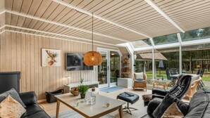 A modern living room with a wooden ceiling, a television, a hanging light fixture, a sofa, a coffee table, and a glass door leading to an outdoor area with chairs and a table. - "Verna" - 800m from the sea by Interhome (Blåvand)