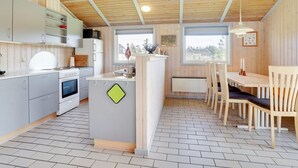 Eine moderne Küche mit weißen Schränken, einem Herd und einer Essecke mit Holztischen und -stühlen.