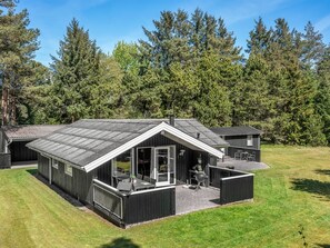 Eine moderne Holzhütte mit geneigtem Dach, großen Fenstern und einer Terrassenfläche.
