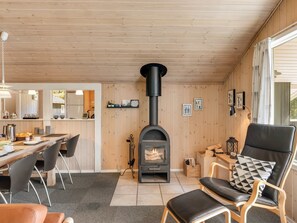Een gezellig interieur van een blokhut, met een houtkachel, een eethoek en een zithoek met open haard.