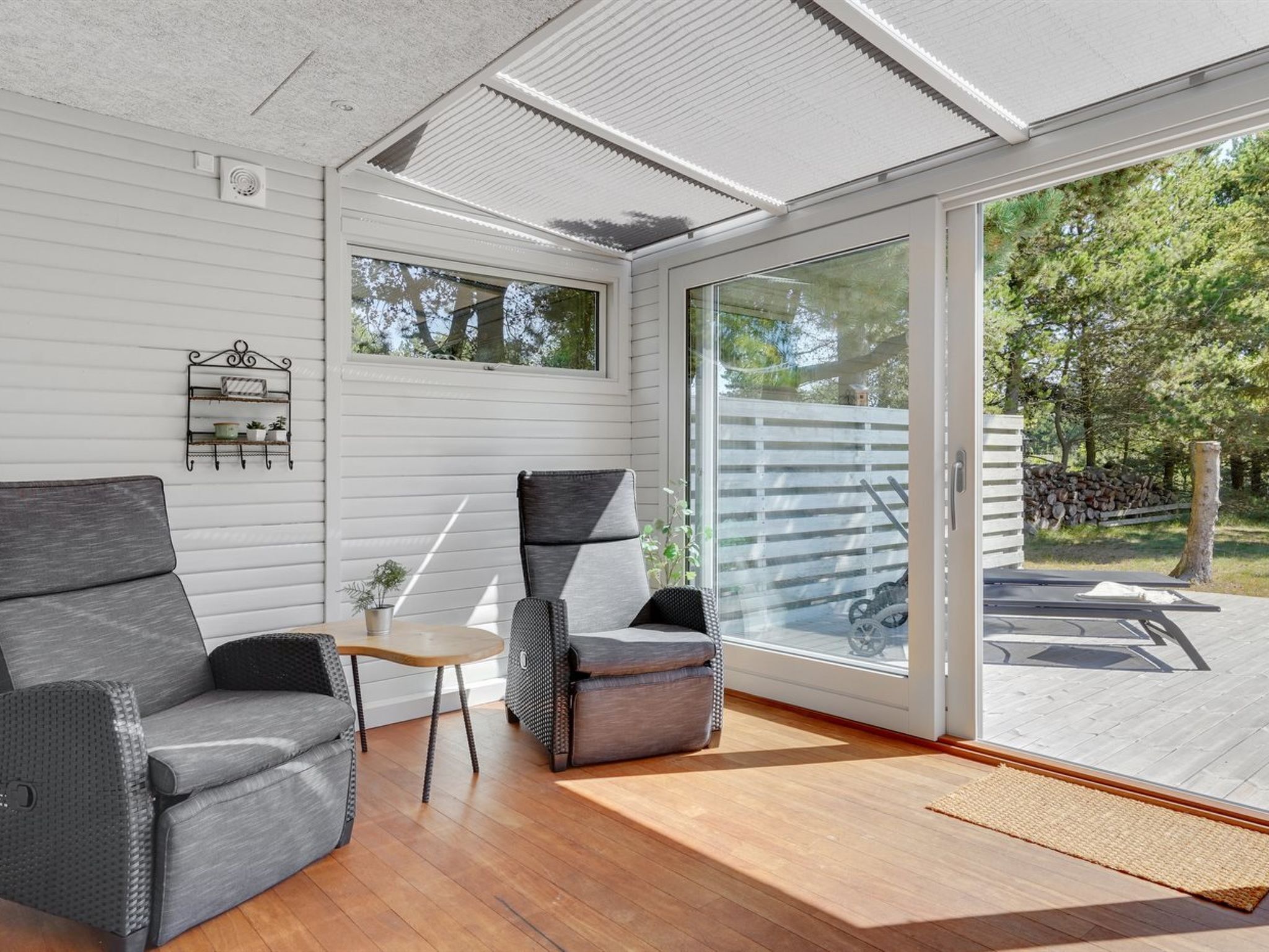 A modern room with a large sliding glass door leading to an outdoor area, a grey sofa, a small table, and a chair.