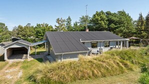 A single-story house with a covered garage, a patio with outdoor seating, and a swing set in the yard.