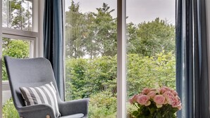 A modern room with a grey armchair, a round ottoman, and a vase of pink flowers on a small table. - "Jörgen" - 100m from the sea by Interhome (Esbjerg V)