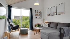 A modern living room with a grey sofa, a black chair, a round ottoman, a small white table with a vase of flowers, and a bookshelf. - "Jörgen" - 100m from the sea by Interhome (Esbjerg V)