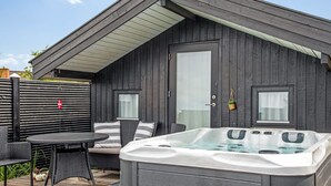 Un bain à remous sur une terrasse en bois, avec un bâtiment en bois aux couleurs sombres en arrière-plan.
