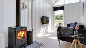Un salon moderne doté d’un poêle à bois, d’un téléviseur à écran plat et d’un coin salon confortable offrant une vue sur l’extérieur.