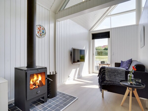 Una sala de estar moderna con estufa de leña, televisor de pantalla plana y una zona de estar acogedora con vistas al exterior.