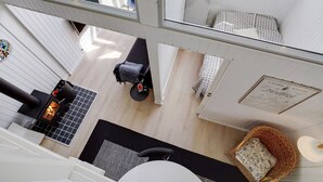 Un espace de vie moderne et compact, doté d’un poêle à bois, d’un petit coin salon et offrant une vue sur la pièce adjacente grâce à une porte en verre.
