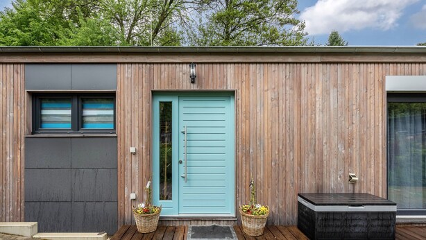 Een modern gebouw met een houten gevel, een blauwe deur en twee plantenmanden.