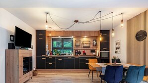 Een moderne keuken met een eethoek, houten kastjes, een groot raam en hanglampen.