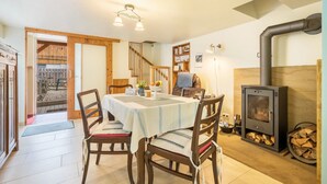 Un comedor con una mesa dispuesta para cuatro, sillas, una escalera de madera, una chimenea y una estantería.