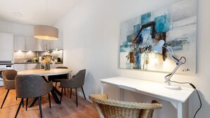 Eine moderne Küche mit weißen Schränken, einem Esstisch mit Stühlen, einer Pendelleuchte und einem Gemälde an der Wand.