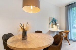 A round wooden dining table with a vase of dried plants, surrounded by upholstered chairs.