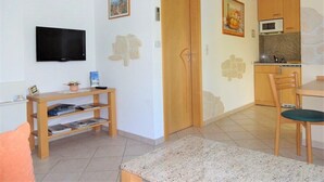 A living room with a TV, wooden furniture, a door, and a kitchen area with cabinets and a microwave. - Apartment 'Ferienwohnung Mit Terrasse, Garten' with Private Terrace, Private Garden and Wi-Fi (Gotha)