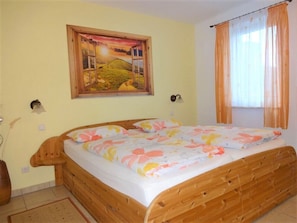 Un dormitorio con una cama de madera, un cuadro de un paisaje y una ventana con cortinas.