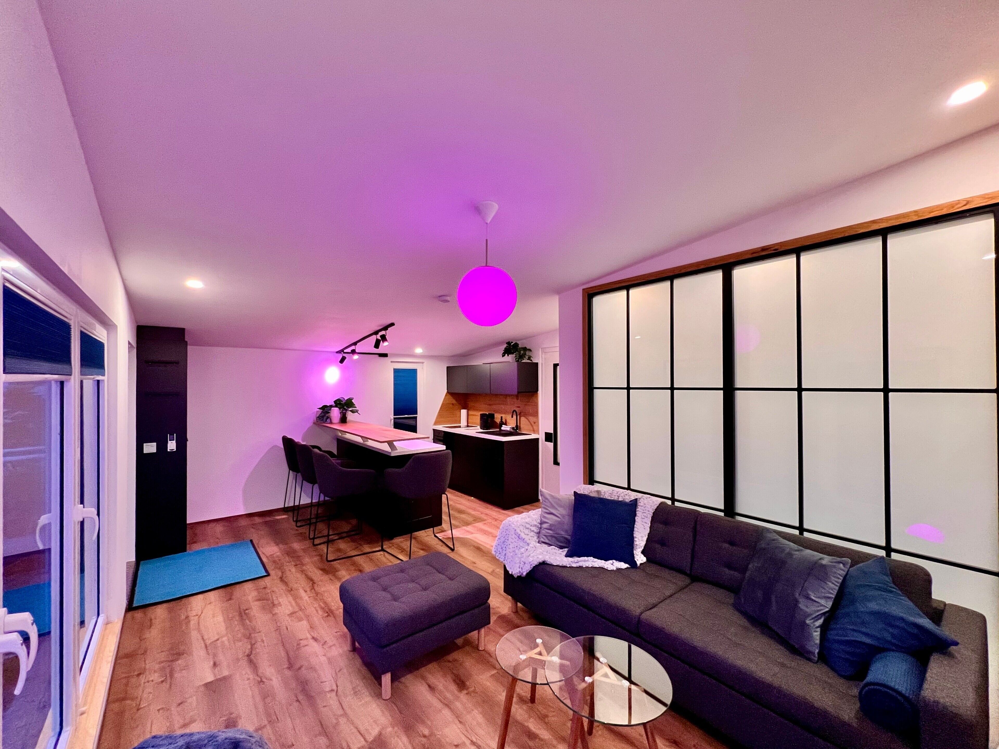 Ein modernes Wohnzimmer mit Sofa, Hocker und einem Essbereich mit Stühlen und Tisch.