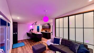 Ein modernes Wohnzimmer mit Sofa, Hocker und einem Essbereich mit Stühlen und Tisch.