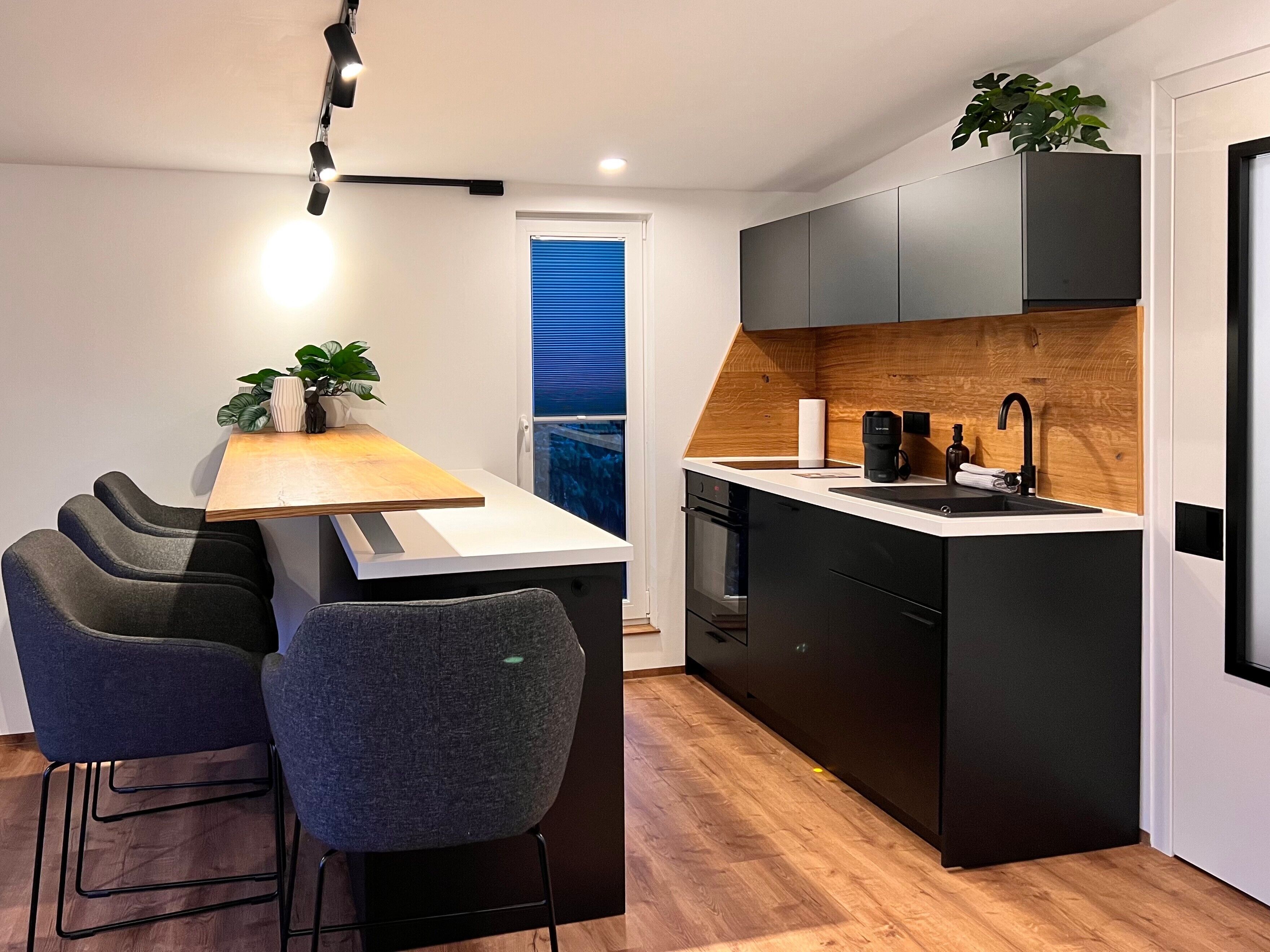 A modern kitchen with a central island, bar stools, a built-in oven, and a wooden accent wall.