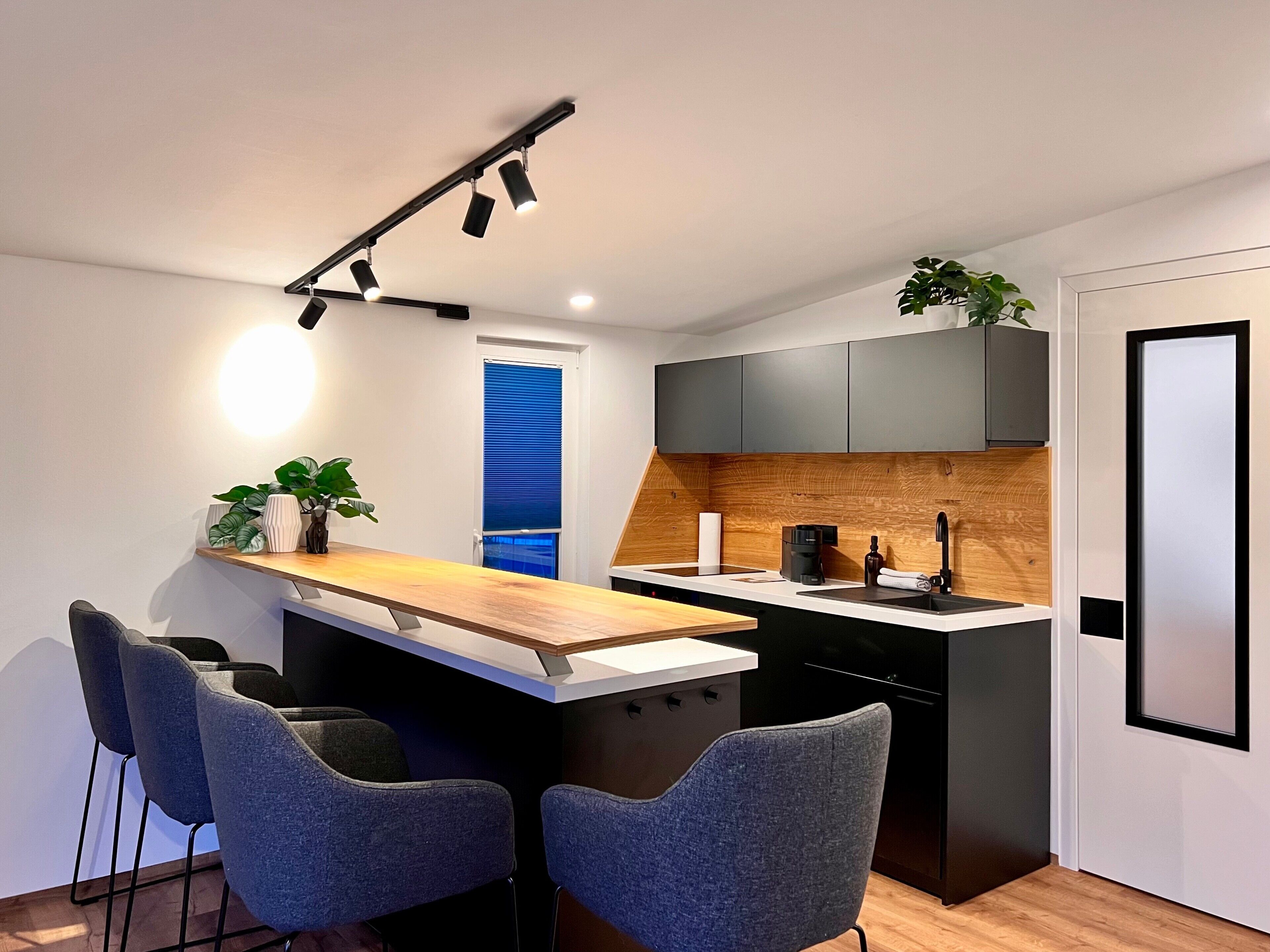 Une cuisine moderne avec un îlot central en bois, des tabourets de bar, une machine à café et un lave-vaisselle encastré.