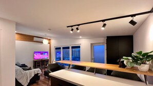A modern kitchen with a wooden countertop, a dining area with chairs, a TV, and a large window with a view.