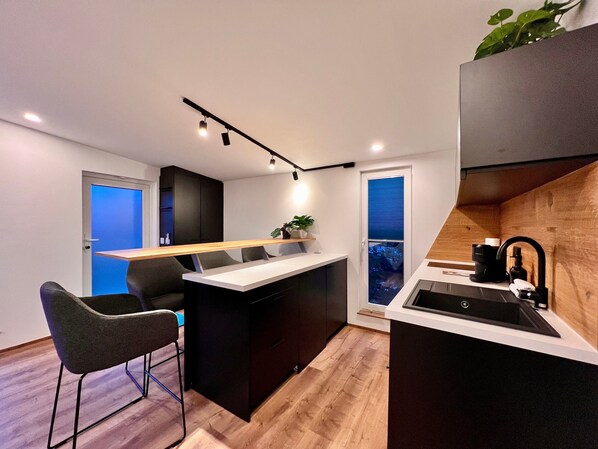 Una cocina moderna con una isla central, taburetes de bar, horno empotrado y ventana con vistas.