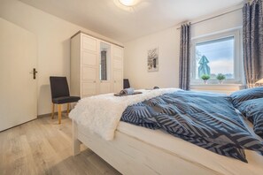 A bedroom with a bed, a chair, a wardrobe, a window with curtains, and a small plant on the windowsill. - Apartment 'Ferienhaus An Der Göhrde' with Private Terrace and Wi-Fi (Zernien)