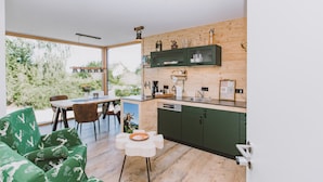 Cocina moderna con armarios de madera, comedor con mesa y sillas, y un ventanal con vistas a zonas verdes.