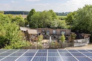 Ein rustikales Holzhaus mit einem umzäunten Garten, Solaranlagen und Blick auf die Landschaft.