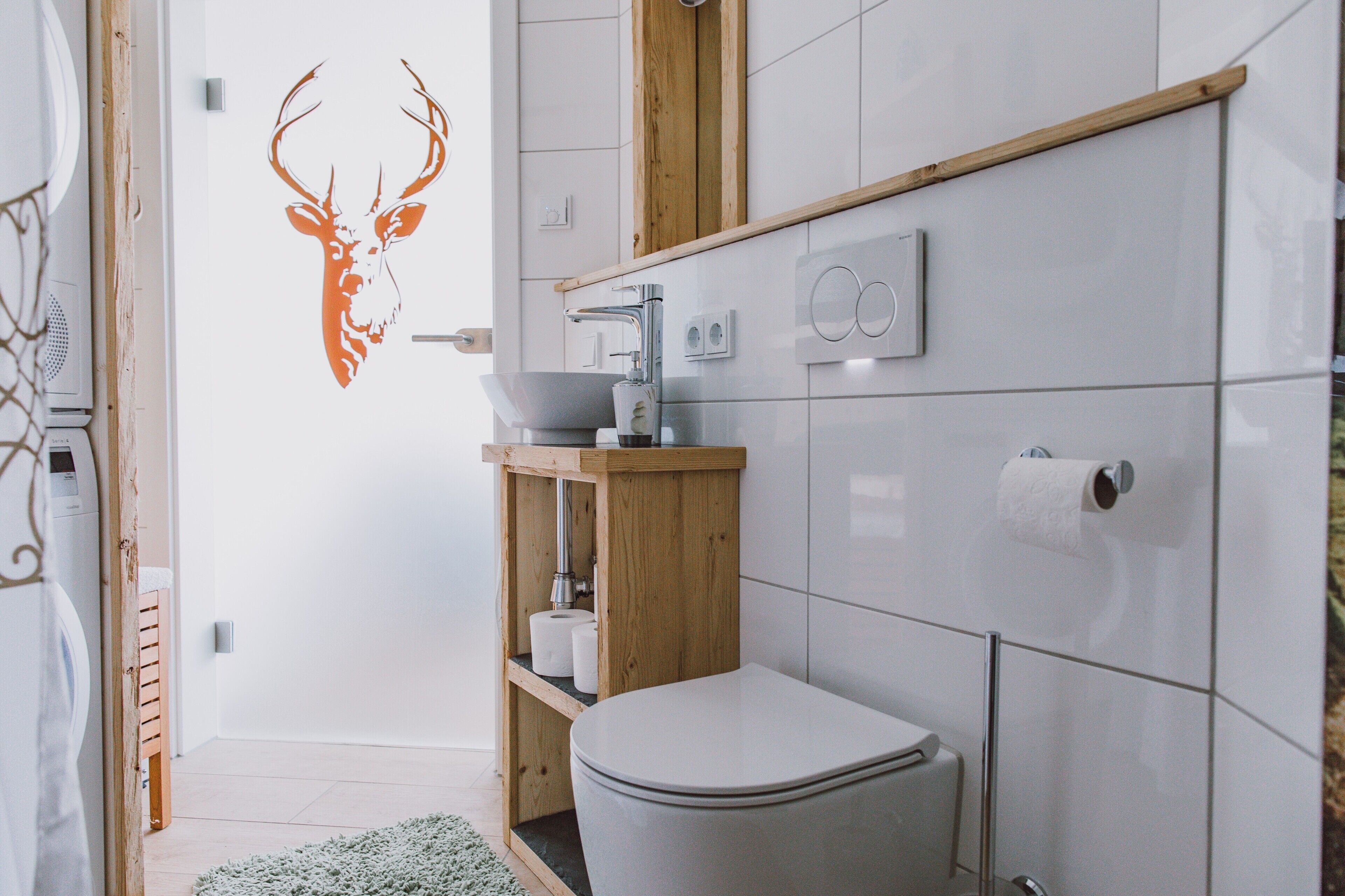 A modern bathroom with a toilet, sink, and wooden shelf.