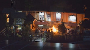 Un área de comedor al aire libre con fuego, estructuras de madera y un cerramiento.