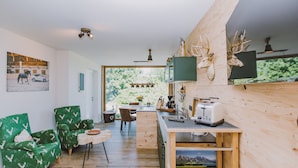 Una cocina moderna con una isla de madera, un comedor con sillas estampadas en verde, y un amplio ventanal que ofrece vistas a la vegetación.
